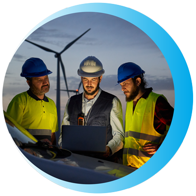 three workers in hard hats reviewing data on a laptop with wind turbines in the background energy management