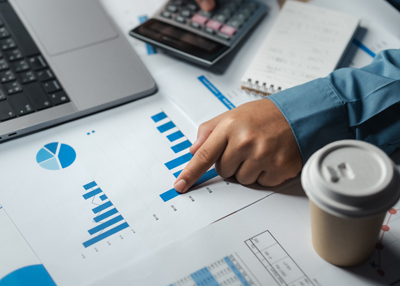 a person pointing at a blue bar graph on a report with a coffee cup and calculator in the background showcasing data analysis techniques and strategies for improving performance