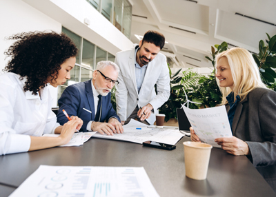 four professionals engaged in a collaborative meeting discussing documents at a table with coffee cups and plants in a modern office setting focusing on effective strategies for group success and planning with six key points